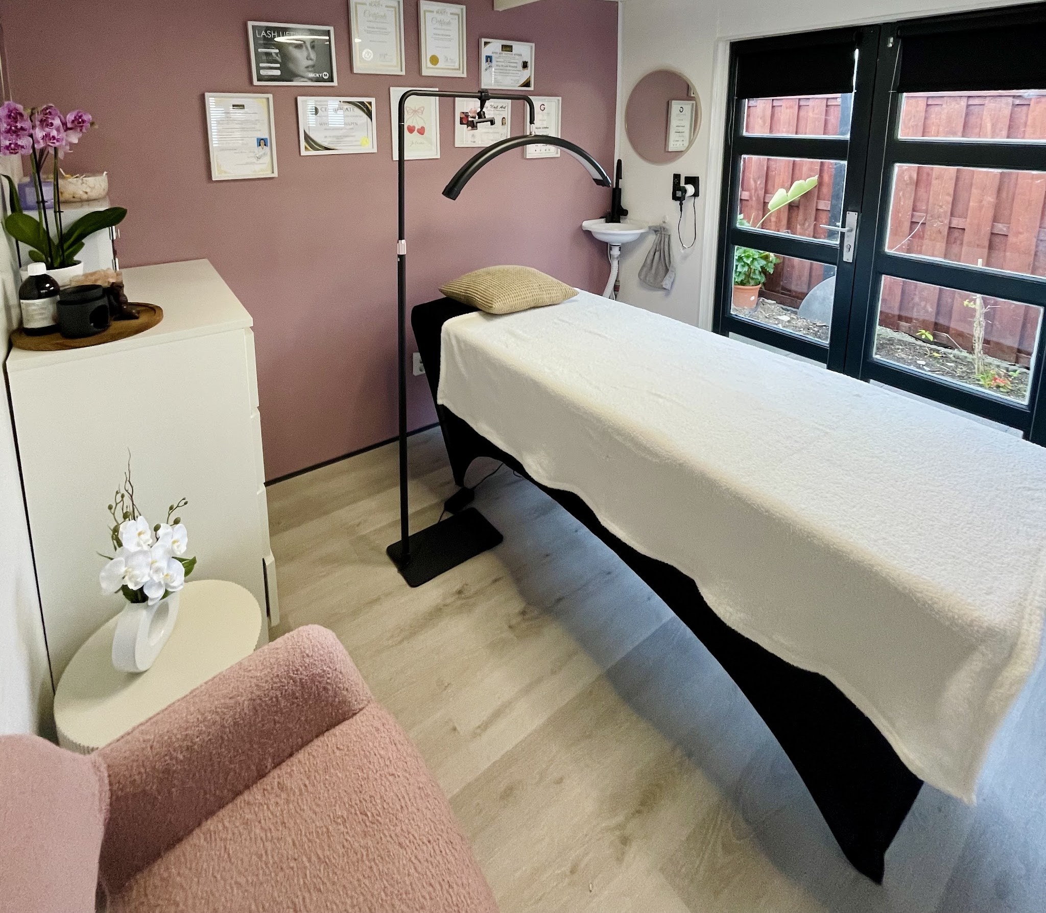 De behandelruimte met de behandeltafel, certificaten aan de mauve wand en de tuindeuren